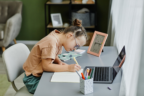 Side view portrait of young girl with down syndrome studying at home and using laptop, copy space