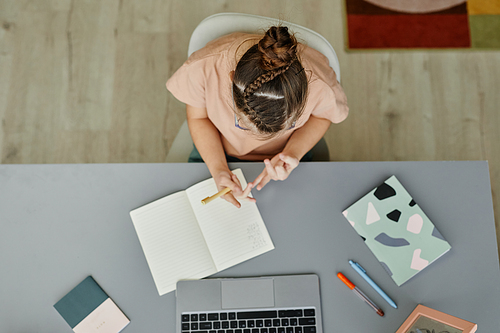 Top view of young girl with down syndrome studying at home while sitting at desk and watching online lesson, copy space