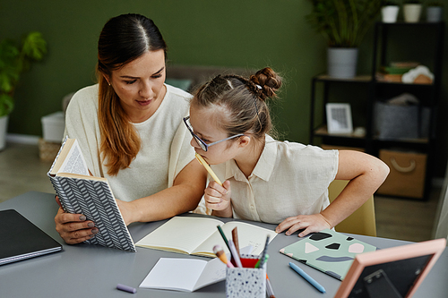 Girl with down syndrome studying at home together with mother or tutor helping