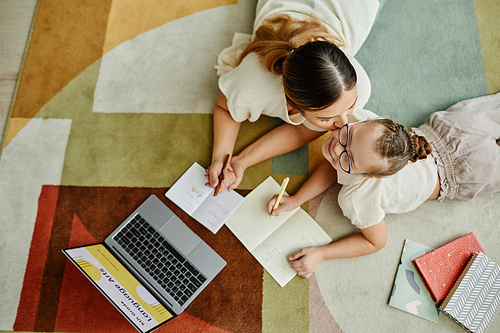 Top view of loving mother kissing daughter with down syndrome studying at home on floor together, non traditional education