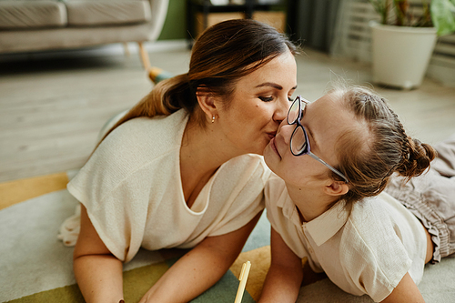 Portrait of loving mother kissing daughter with down syndrome while laying on floor together, non traditional family