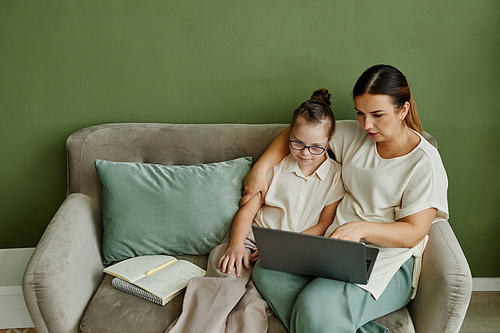 Minimal portrait of mother and daughter with down syndrome relaxing on couch together in cozy home, copy space