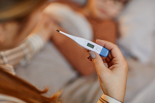 Closeup of unrecognizable mother holding thermometer while caring for sick child at home, copy space