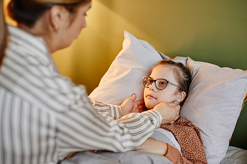 Portrait of caring mother tucking in child with down syndrome at bedtime, copy space