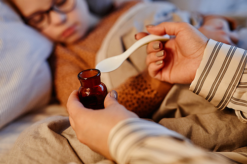 Close up of unrecognizable mother giving medicine to sick child recovering at home, copy space