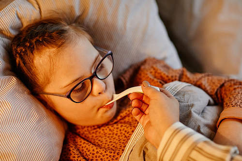 Portrait of young girl with down syndrome taking medicine while recovering in bed at home, copy space