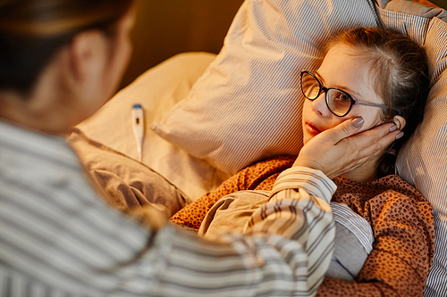 Portrait of loving mother caring for sick child with down syndrome suffering from fever at night in warm lamplight