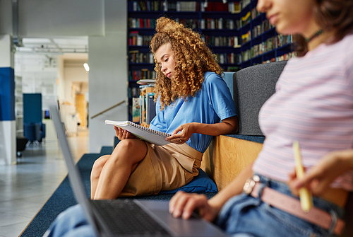 Vibrant side view portrait of young girl with curly hair studying in college library