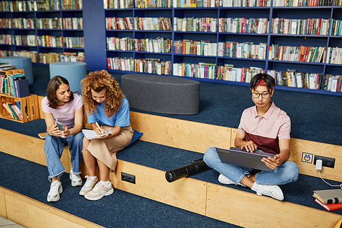 Vibrant full length shot of diverse group of students in college library doing homework, copy space