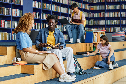 Diverse group of college students in library lounge, focus on black young man talking to friend