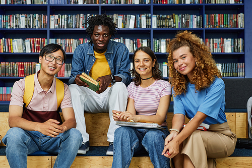 Front view at diverse group of students in library smiling happily at camera against bookshelves