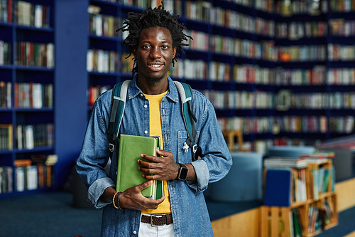 Waist up portrait of black young man with backpack standing in library and looking at camera, copy space