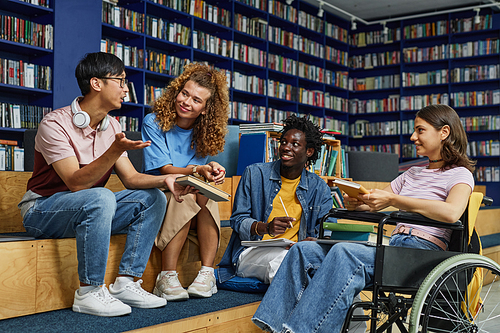 Diverse group of students in college library including young woman in wheelchair enjoying discussion