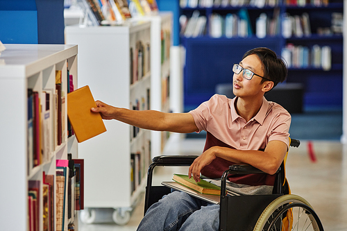 Portrait of Asian student with disability choosing books in college library with accessibility features