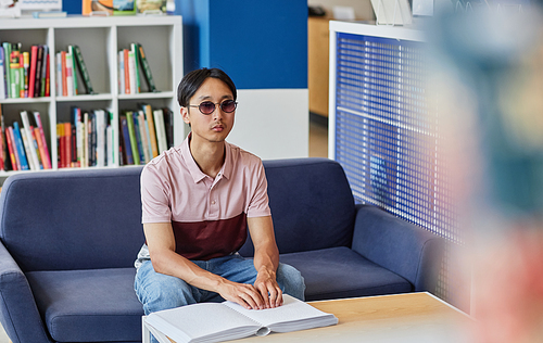 Portrait of blind Asian man reading book in tactile braille and wearing sunglasses, copy space