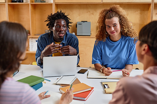 Diverse group of young students working on project together while sitting at table, focus on African American American man speaking