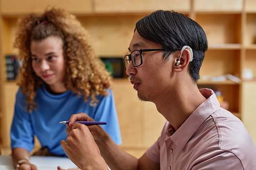 Side view portrait of young Asian man speaking to group of students in library, copy space