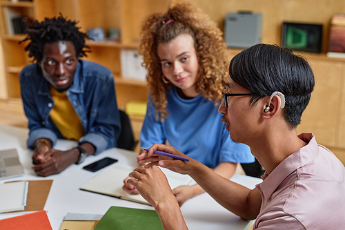 High angle portrait of young Asian man speaking to group of students in library, copy space