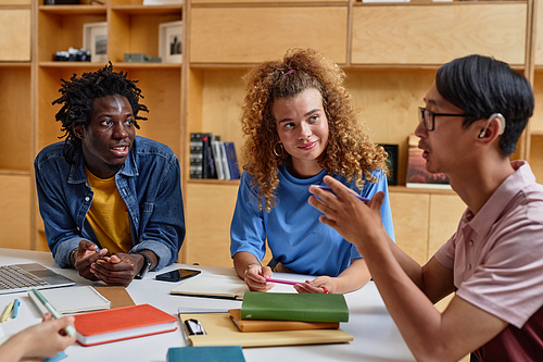 Diverse group of students working in library together, focus on smiling young woman with curly hair