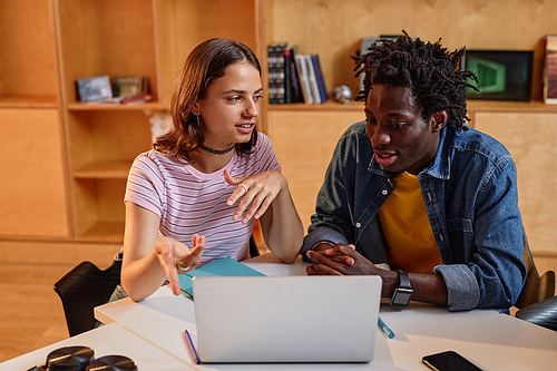 Portrait of two young students working together in library and using laptop