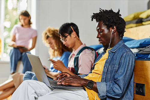 Diverse group of students in row studying, focus on African American young using laptop in foreground