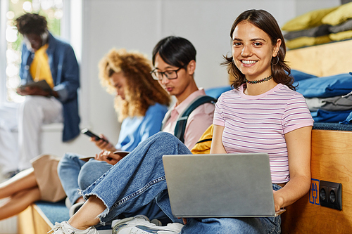 Diverse group of students in row studying, focus on smiling young woman using laptop in foreground, copy space