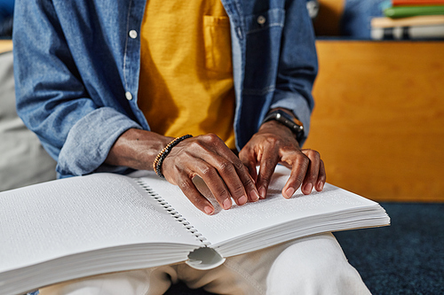 Close up of blind African American man reading book in braille in college library lounge