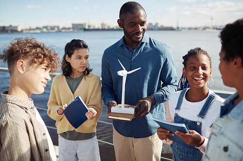Portrait of black male teacher demonstrating wind mill model to group of kids during outdoor class in sunlight