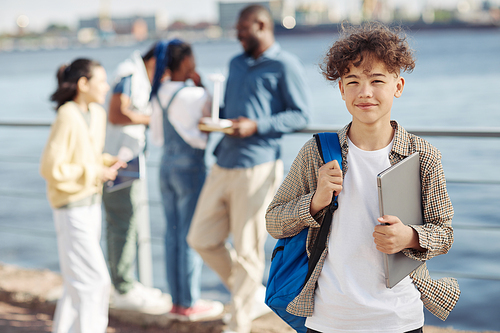 Waist up portrait of smiling teenage boy with backpack posing during outdoor class, copy space