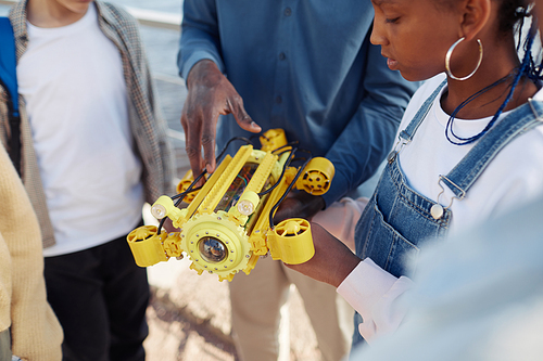 Close up of young black girl holding robot model during engineering class outdoors with teacher helping