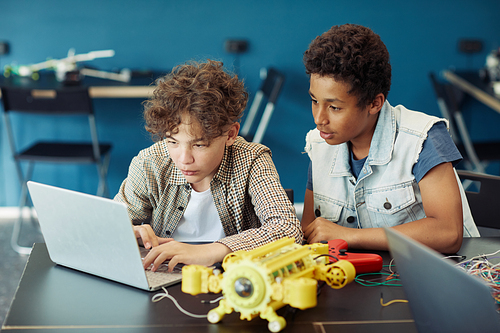 Portrait of two teenage boys using laptop and programming robot during engineering class in school