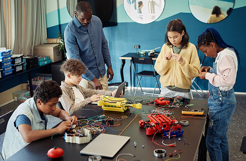 Diverse group of teenage children building robots together while enjoying engineering class in modern school