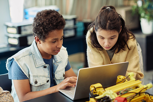Portrait of boy and girl using laptop together and programming robots during engineering class at school