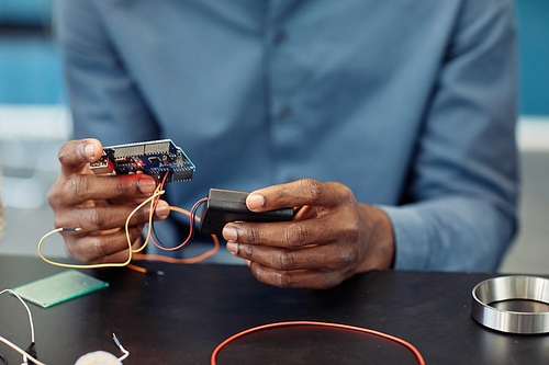 Close up of black young man holding circuit board while building robot, copy space