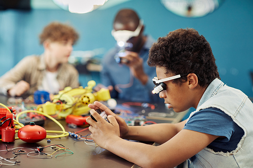 Side view portrait of young black boy building robots in engineering class at school, copy space