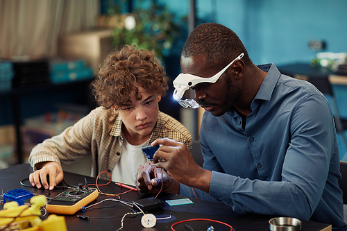 Portrait of young teenage boy building robots in engineering class with male teacher helping