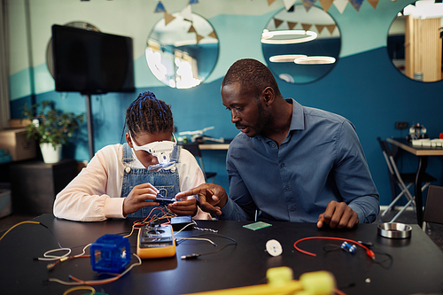 Portrait of black teen girl building robot in engineering class with male teacher helping