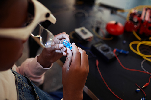 Close up of black young boy holding circuit chip while building robot in engineering class, copy space