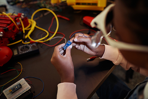 Close up of kid holding circuit chip while building robot in engineering class, copy space