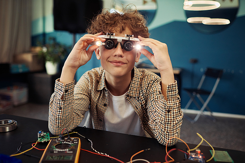 Portrait of smiling boy wearing magnifying glasses with lights while enjoying robotics and engineering class at school