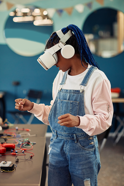 Vertical portrait of black teenage girl using VR technology in engineering class and looking around