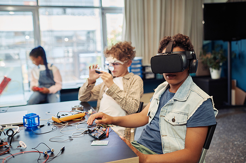 Portrait of two children building robots in engineering class and using VR technology