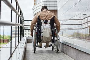 Back view of man with disability pushing wheelchair wheel while going down ramp in city, copy space