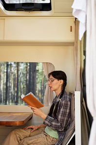 Young girl in eyeglasses reading a book sitting in house of wheels during trip