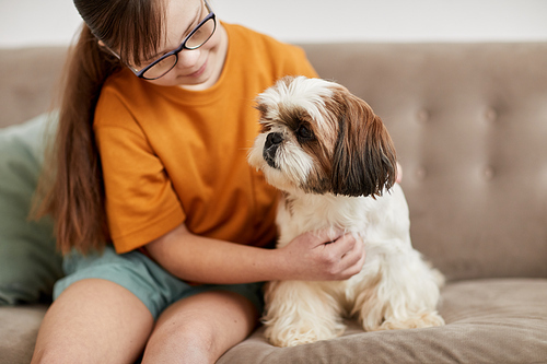 Portrait of cute girl with Down syndrome playing with small dog while sitting on couch together, copy space