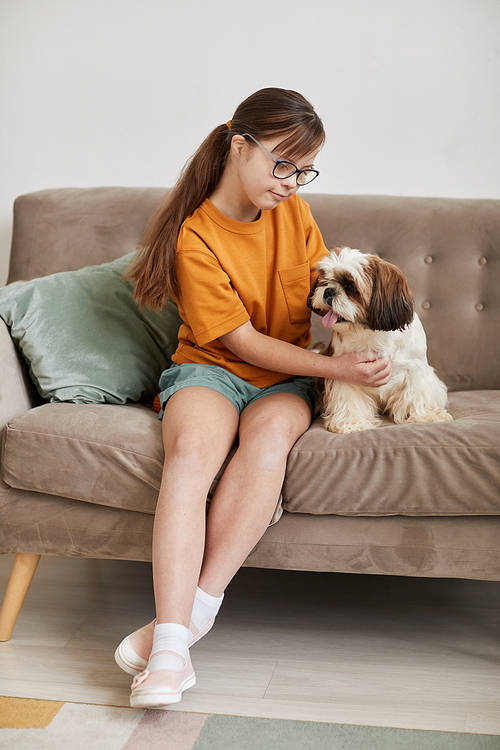 Full length portrait of teenage girl with Down syndrome playing with small dog while sitting on couch together