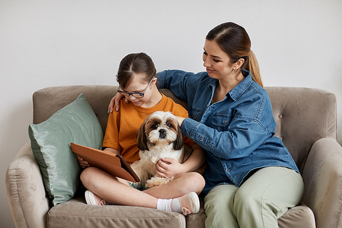 Minimal portrait of caring mother and daughter with Down syndrome sitting on couch with cute dog
