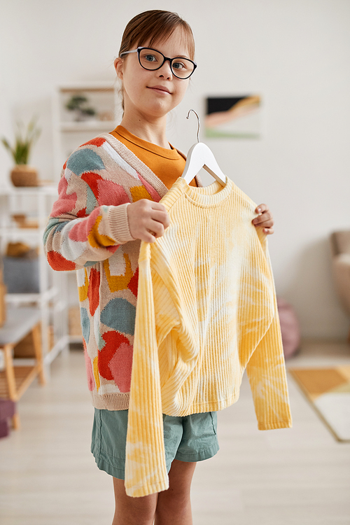 Vertical portrait of young teenage girl with Down syndrome choosing clothes and looking at camera