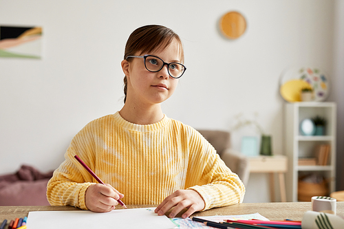 Minimal portrait of teenage girl with Down syndrome drawing pictures at table and looking away