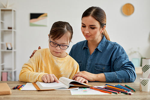 Portrait of mother and daughter with Down syndrome reading book together during adapted homeschooling lesson